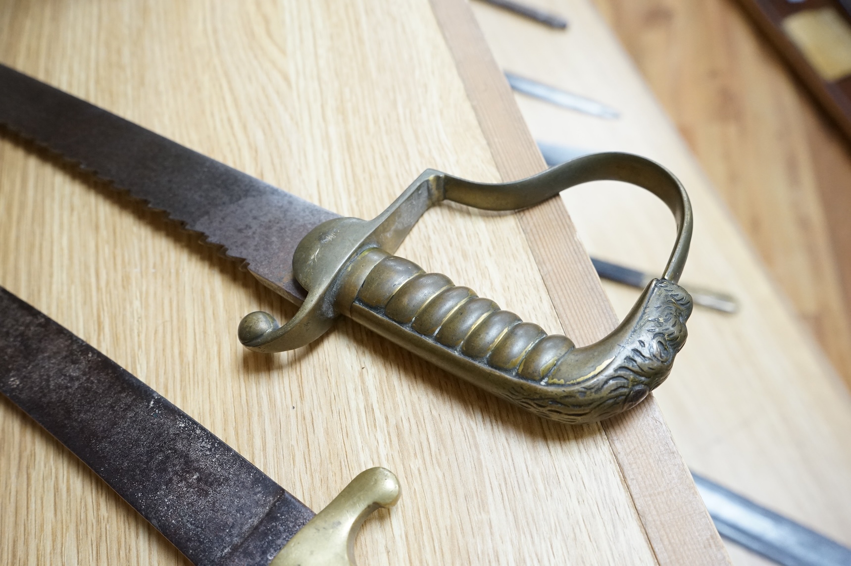 A British Pioneer’s sidearm with brass stirrup hilt, lion’s head pommel and sawback blade, together with an Imperial German sidearm with one piece brass hilt and slightly curved single edge blade